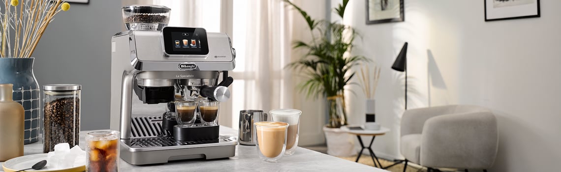 De’Longhi La Specialista Espresso­maschine in moderner Küche, mit frisch gebrühten Espressi und Milchgetränken auf dem Tisch.