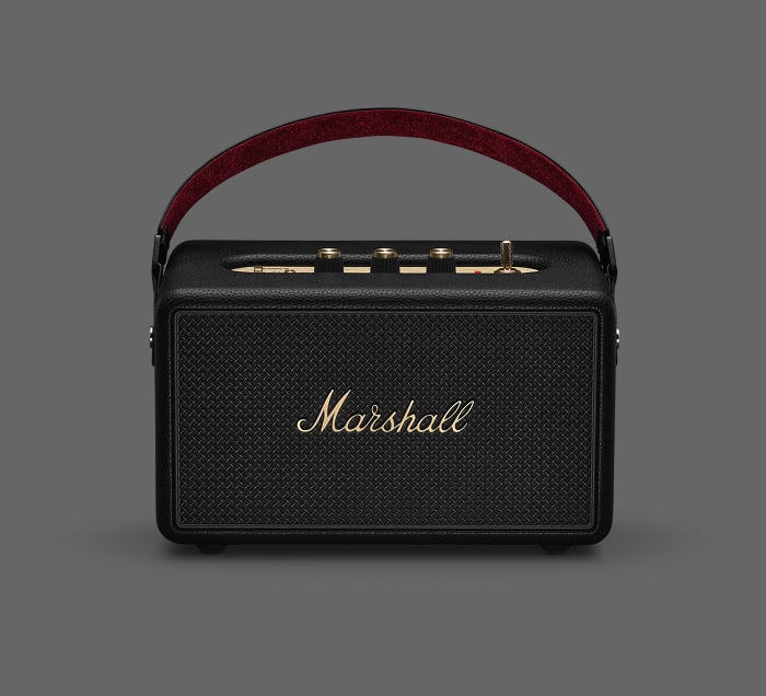 Marshall Kilburn III Bluetooth-Lautsprecher in Schwarz mit rotem Tragegriff und goldenen Bedienelementen auf grauem Hintergrund.