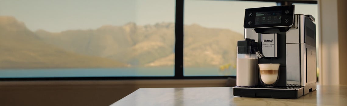 De’Longhi PrimaDonna Kaffeevollautomat auf Küchentresen mit Bergpanorama im Hintergrund – perfekter Kaffeegenuss in Premiumqualität.