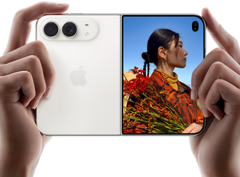 iPhone Duo, Farbe Sternenweiß, in zwei Händen im Querformat gehalten, aufgefaltet, linke Seite mit 48 MP Dual Fusion Rückkameras, rechte Seite zeigt eine Person, die fotografiert wird, auf dem äußeren Display kann die fotografierte Person während der Aufnahme mit Duo Preview ihr Gesicht sehen