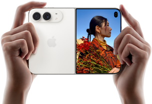 iPhone Duo, Farbe Sternenweiß, in zwei Händen im Querformat gehalten, aufgefaltet, linke Seite mit 48 MP Dual Fusion Rückkameras, rechte Seite zeigt eine Person, die fotografiert wird, auf dem äußeren Display kann die fotografierte Person während der Aufnahme mit Duo Preview ihr Gesicht sehen